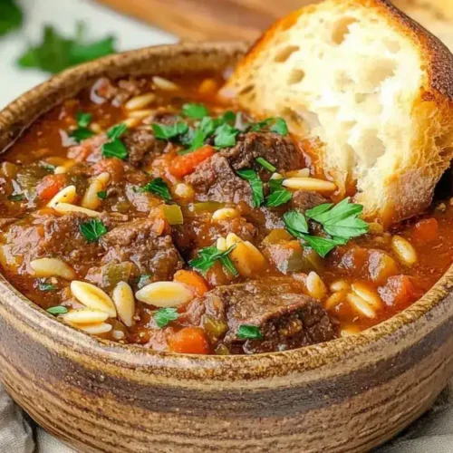 A hearty bowl of Beef Minestrone Soup recipe with tender beef chunks, vegetables, orzo pasta, and a slice of toasted bread on the side.