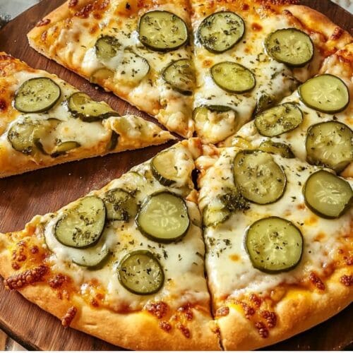 A freshly baked pickle pizza with melted cheese and sliced pickles on a wooden serving board.