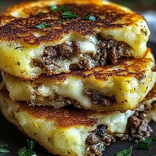 A stack of Potato Pancakes with Savory Beef and Cheese filled with seasoned beef and melted cheese, garnished with fresh herbs.