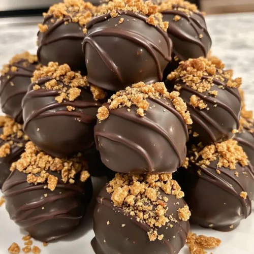 Close-up of Butterfinger Balls stacked on a white plate, coated in rich chocolate and topped with crushed Butterfinger candy.