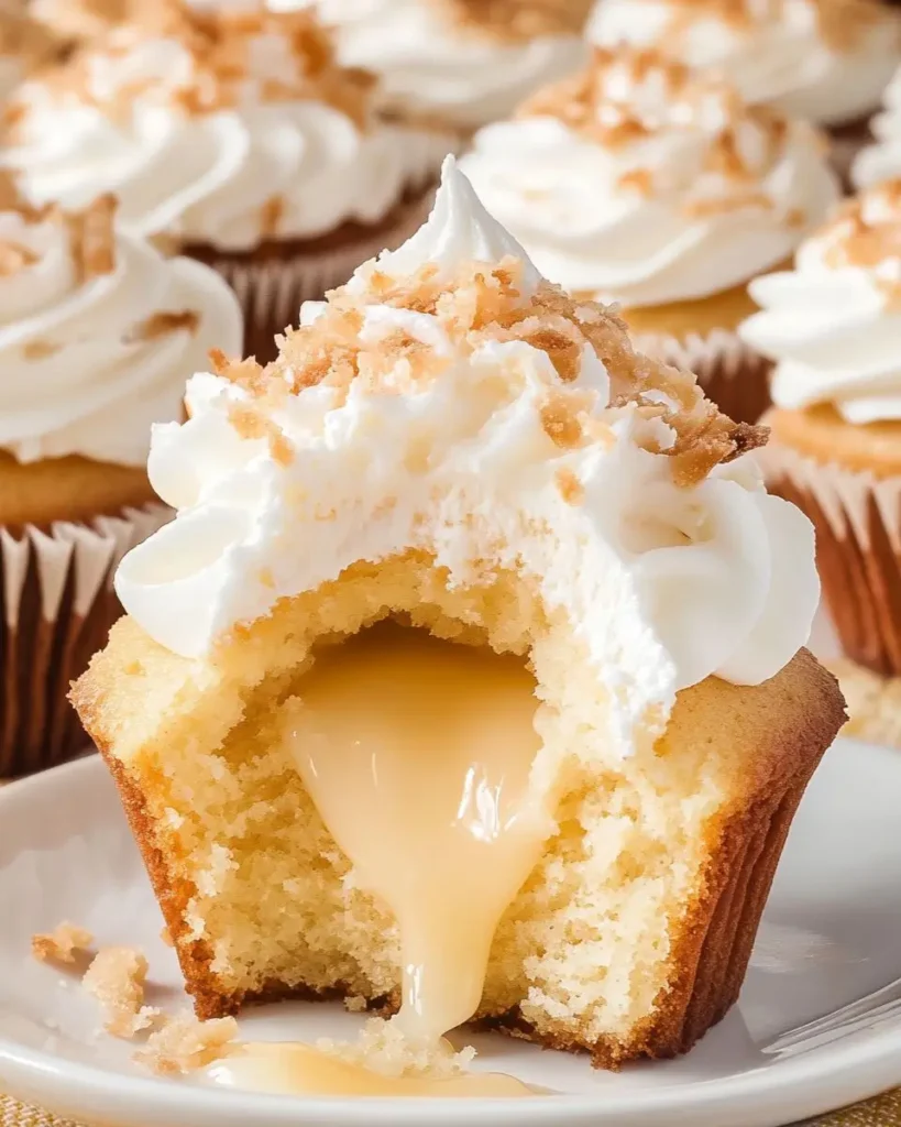 Close-up of a Coconut Cream Pie Cupcakes with a creamy coconut filling oozing from the center, topped with whipped frosting and toasted coconut flakes.
