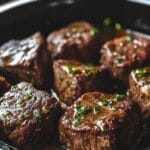 Tender crockpot steak bites simmered in a savory garlic herb sauce inside a slow cooker.