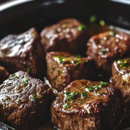 Tender crockpot steak bites simmered in a savory garlic herb sauce inside a slow cooker.