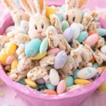 A festive bowl of Easter Bunny Bait snack mix with candy-coated eggs, cookie pieces, and bunny-shaped sweets in a pink bowl.