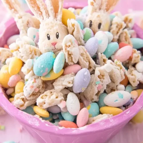 A festive bowl of Easter Bunny Bait snack mix with candy-coated eggs, cookie pieces, and bunny-shaped sweets in a pink bowl.
