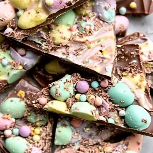 Colorful Easter egg chocolate bark with pastel candies and chocolate shavings on a marble background.