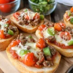 Mini garlic toast pizzas topped with ground beef, green bell peppers, cherry tomatoes, and melted cheese.