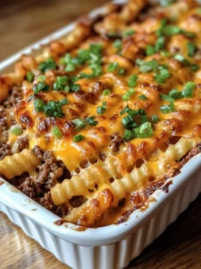 A cheesy cheeseburger French fry casserole topped with crinkle-cut fries, ground beef, melted cheddar, and chopped green onions in a white baking dish.