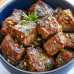 Juicy garlic butter steak bites garnished with chopped herbs served in a blue bowl.