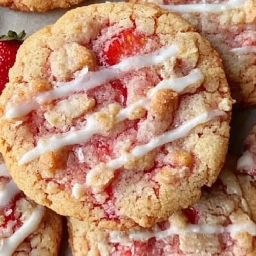 Freshly baked strawberry crunch cookies drizzled with white icing, showcasing a golden-brown texture and vibrant strawberry pieces.