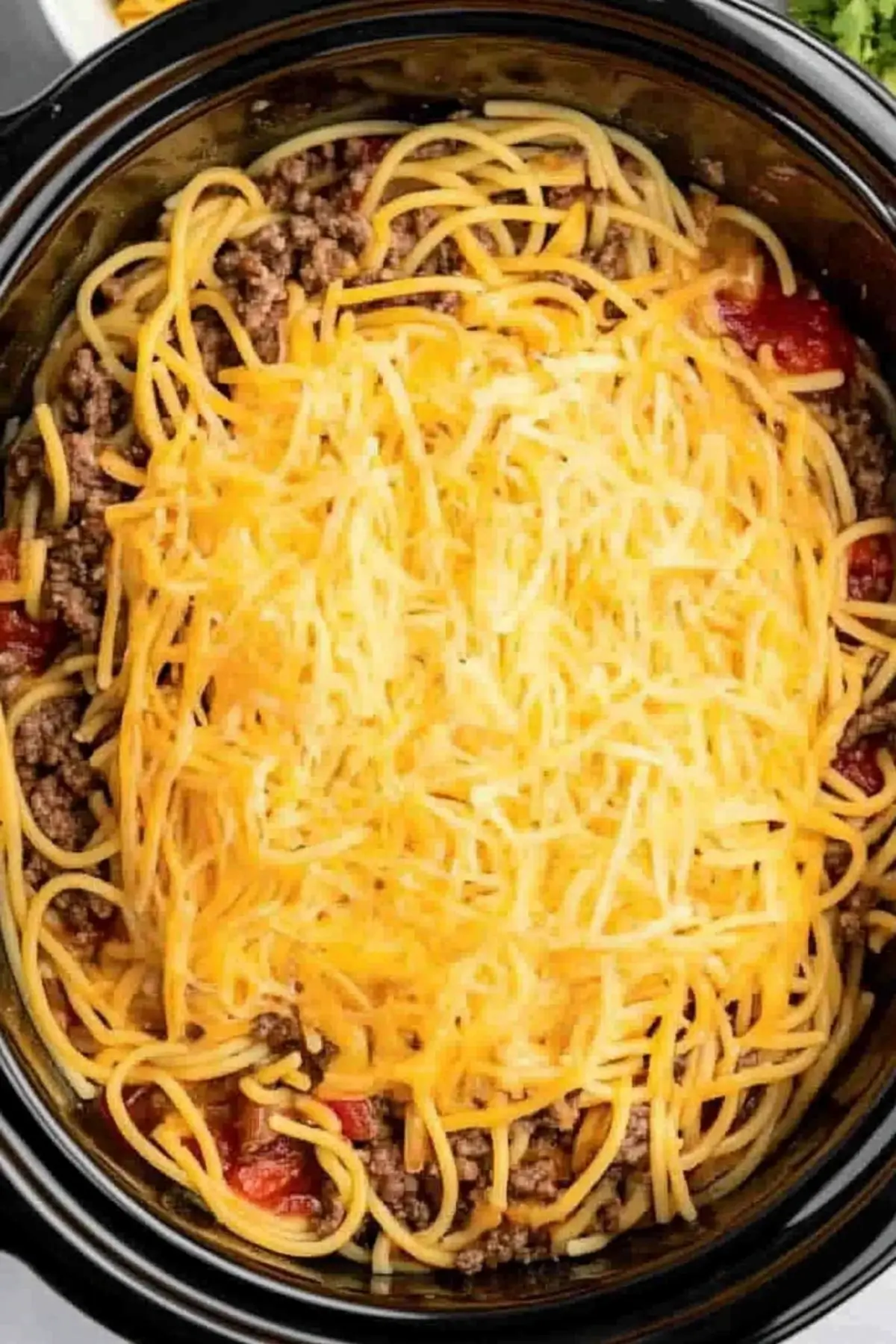 Healthy taco spaghetti Overhead view of healthy taco spaghetti in a slow cooker, featuring cooked spaghetti noodles topped with melted cheese, seasoned lean ground beef, and diced tomatoes visible around the edges.