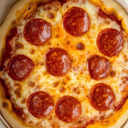 A homemade pepperoni Slow Cooker Pizza, showing golden melted cheese, perfectly arranged pepperoni slices, and a golden-brown crust, all contained within a white slow cooker lined with parchment paper.
