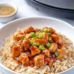 Bowl of Sweet Hawaiian Crockpot Chicken Recipe featuring glazed chicken pieces in a rich sauce served over rice, topped with green onions, with a crockpot visible in the background.