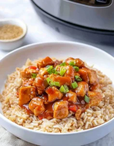 Bowl of Sweet Hawaiian Crockpot Chicken Recipe featuring glazed chicken pieces in a rich sauce served over rice, topped with green onions, with a crockpot visible in the background.