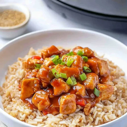 Bowl of Sweet Hawaiian Crockpot Chicken Recipe featuring glazed chicken pieces in a rich sauce served over rice, topped with green onions, with a crockpot visible in the background.