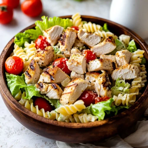 Grilled Chicken Caesar Pasta Salad served in a wooden bowl with cherry tomatoes, romaine lettuce, and rotini pasta.