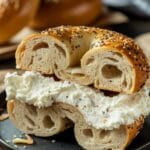 Sliced everything bagel filled with creamy whipped Cottage Cheese Bagels spread, served on a black plate. A perfect example of Cottage Cheese Bagels.
